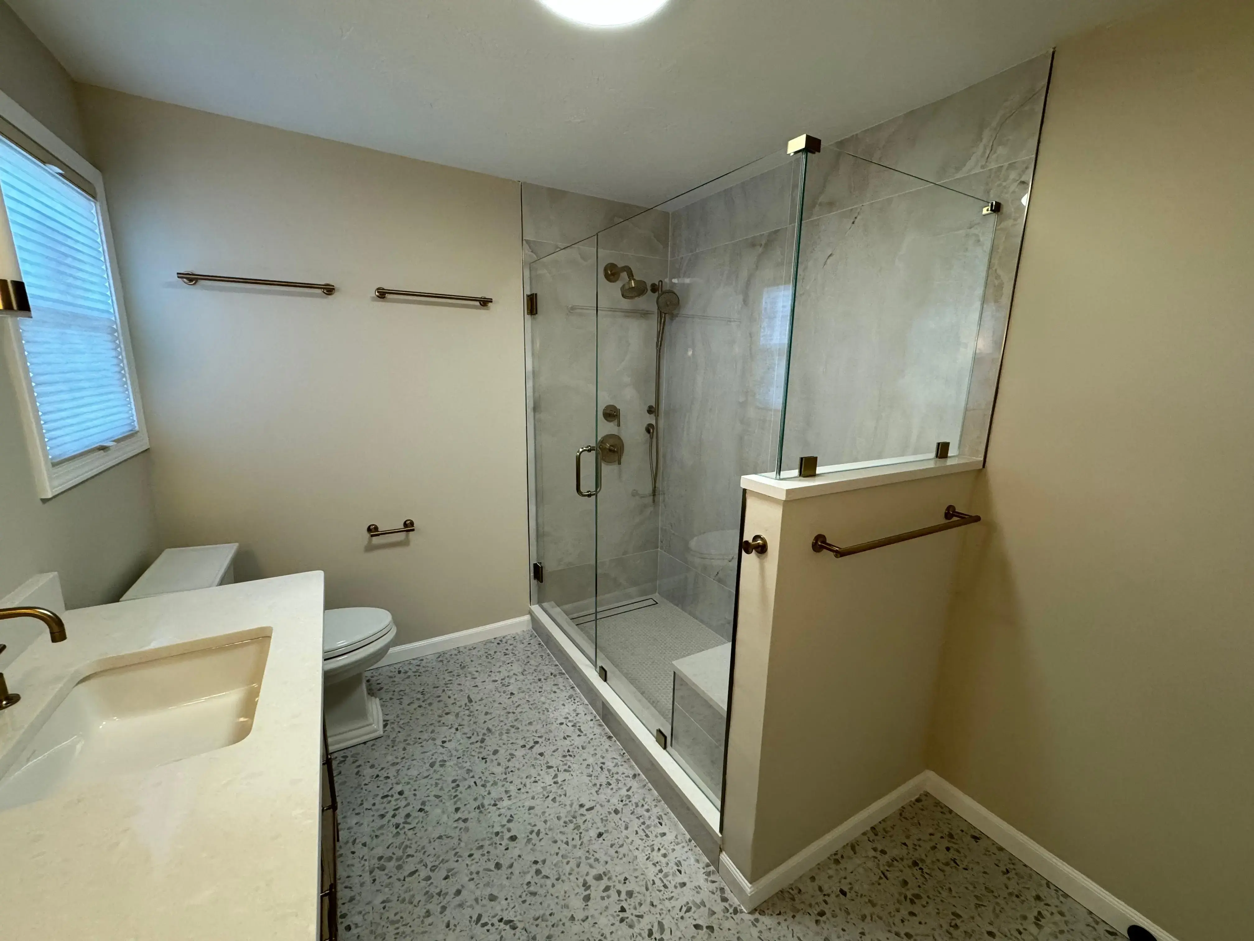 Custom glass shower enclosure with gray marble tile walls and brass hardware.