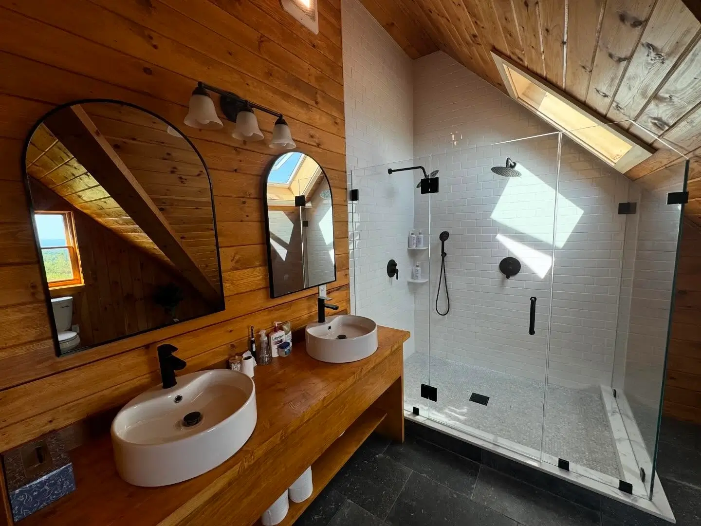 Arched mirrors and double vessel sinks on wood vanity in a rustic bathroom.