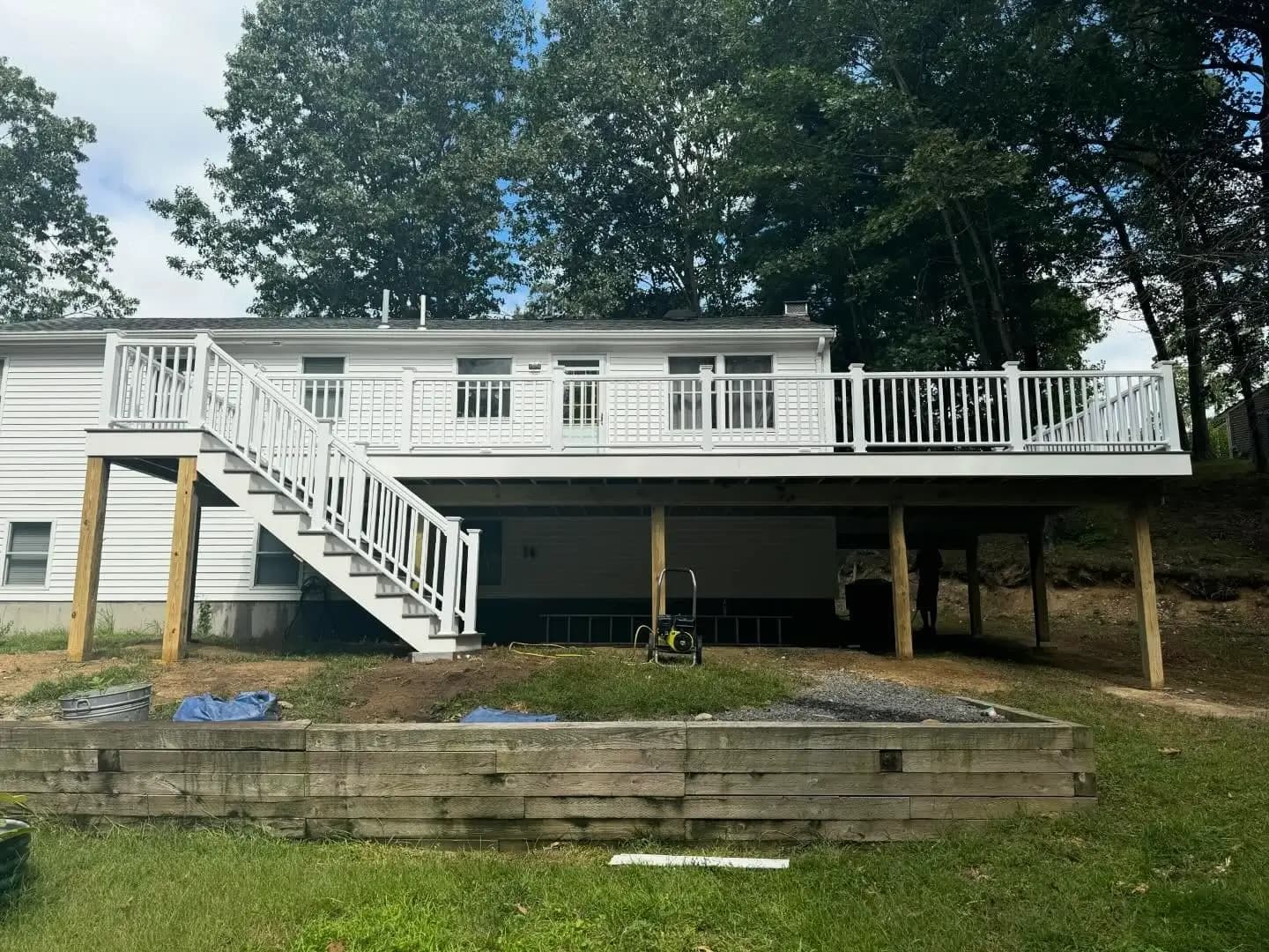 Elevated backyard composite deck with stairs leading down to lawn and white siding house.