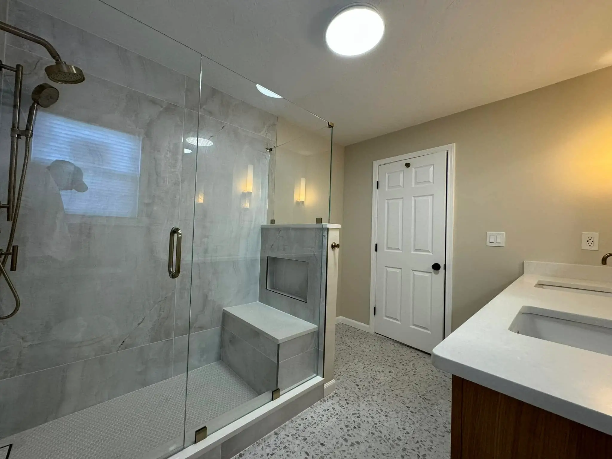 Walk-in custom glass shower enclosure with gray marble tile wall and bench.