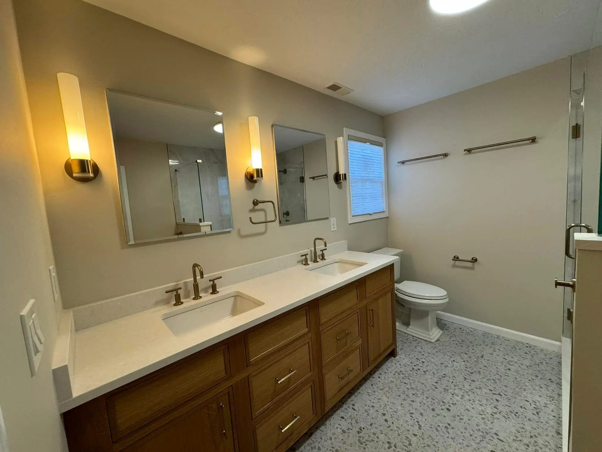 Double vanity with wood cabinets, gold faucets, and mirrors in primary bathroom.