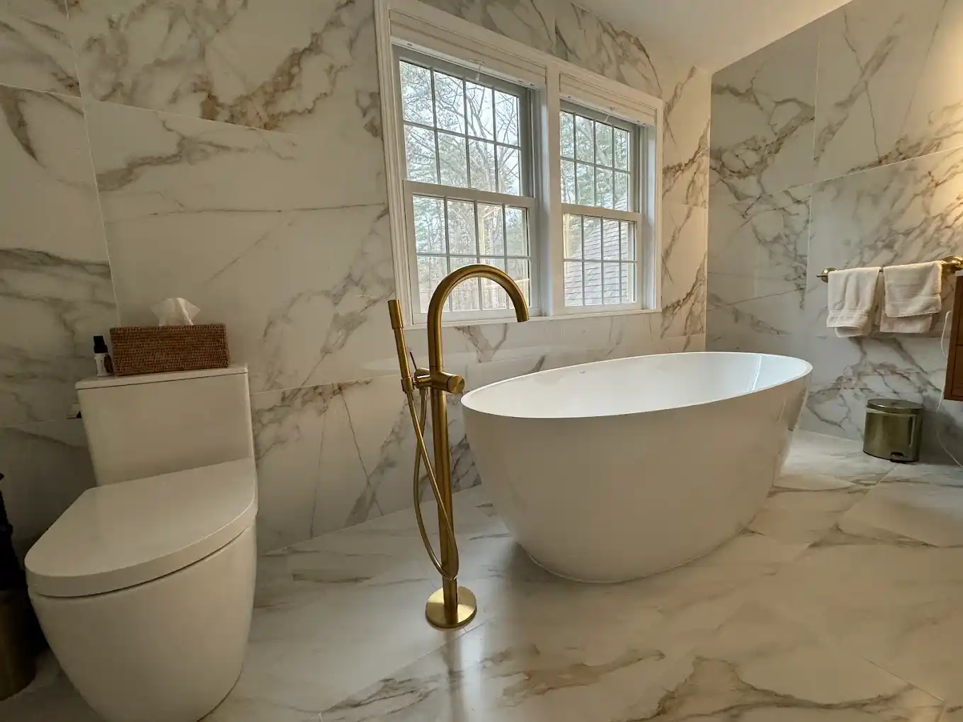 Primary bathroom featuring marble wall tiles, freestanding tub, and gold faucet.