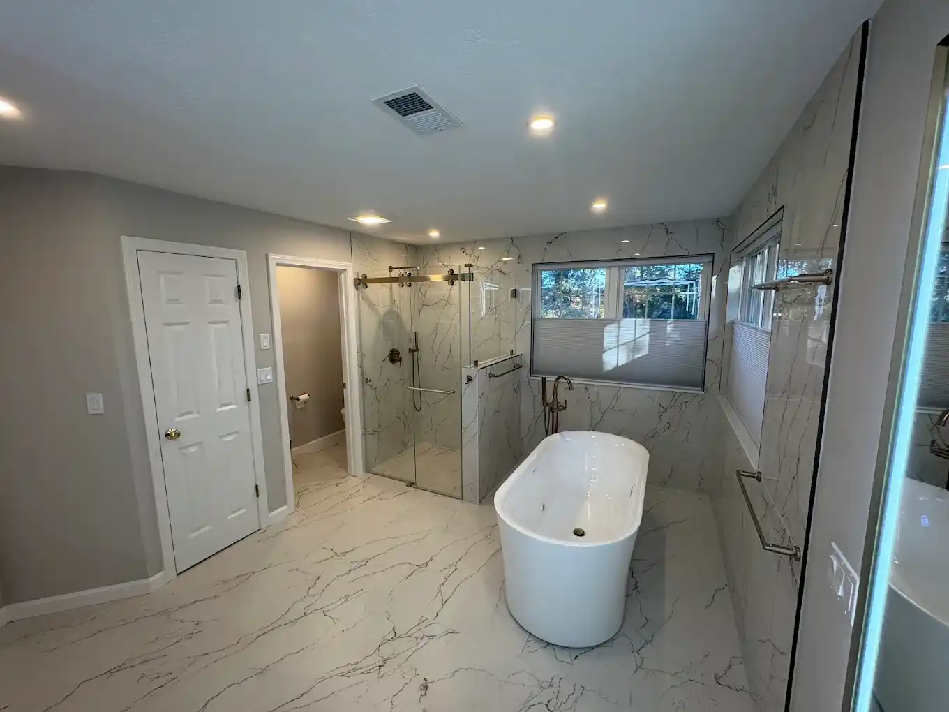 Luxury master bathroom with freestanding soaking tub, walk-in glass shower, and marble tile.