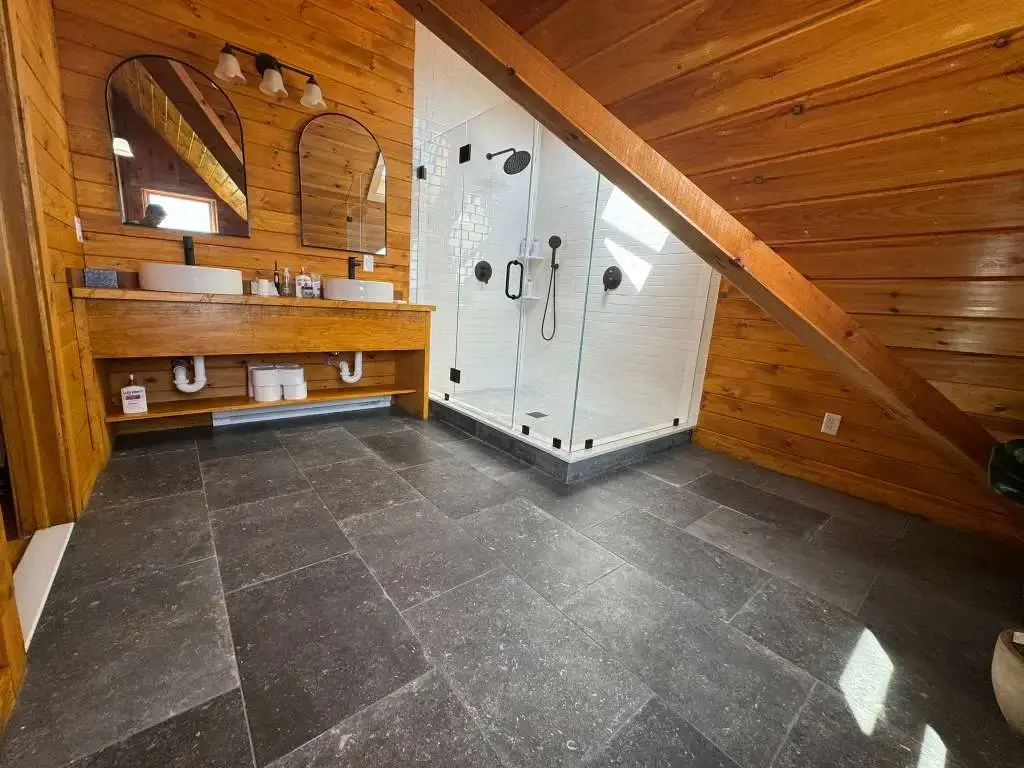 Glass walk-in shower with white subway tile and dark slate floor tiles in a rustic bathroom.